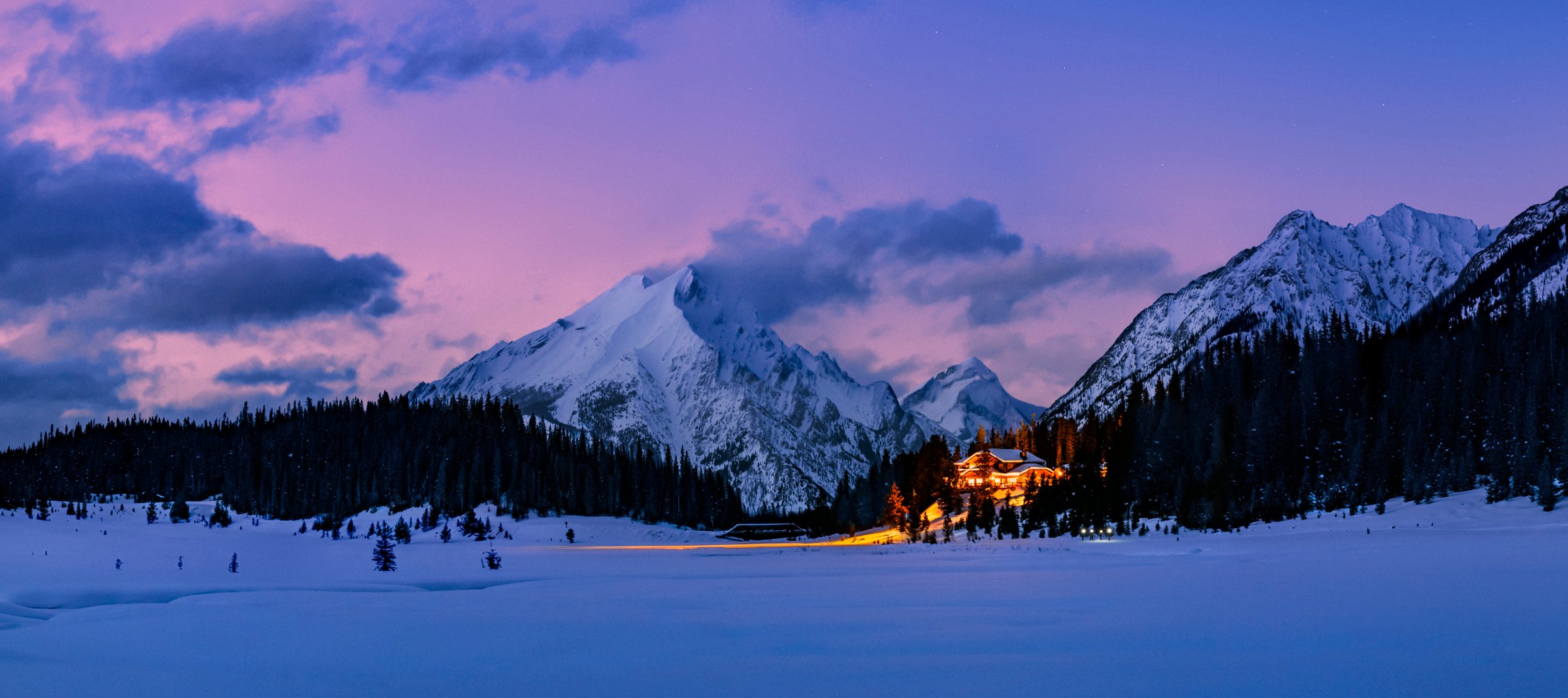 A large lodge lit up at dusk under a pink-blue sky.