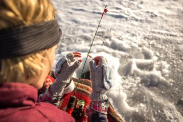 Looking over a woman's shoulder as she prepares her fishing rod to go ice fishing