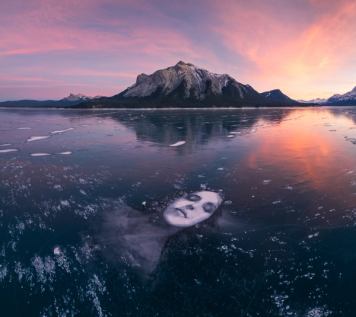 A 60-foot charcoal portrait of a relaxed woman stretches across Abraham Lake at sunset with the Canadian Rockies at the shoreline.