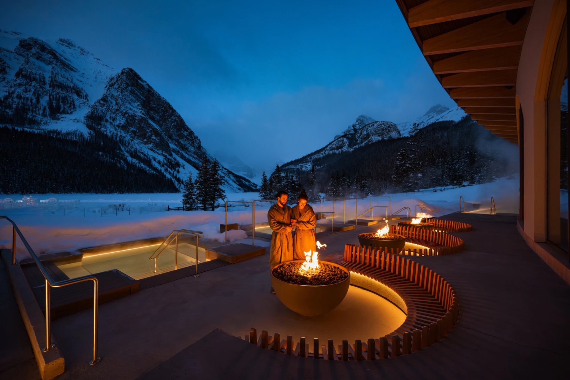 A couple relax outdoors among the pools and firepits at BASIN Glacial Waters Spa at Fairmont Chateau Lake Louise.