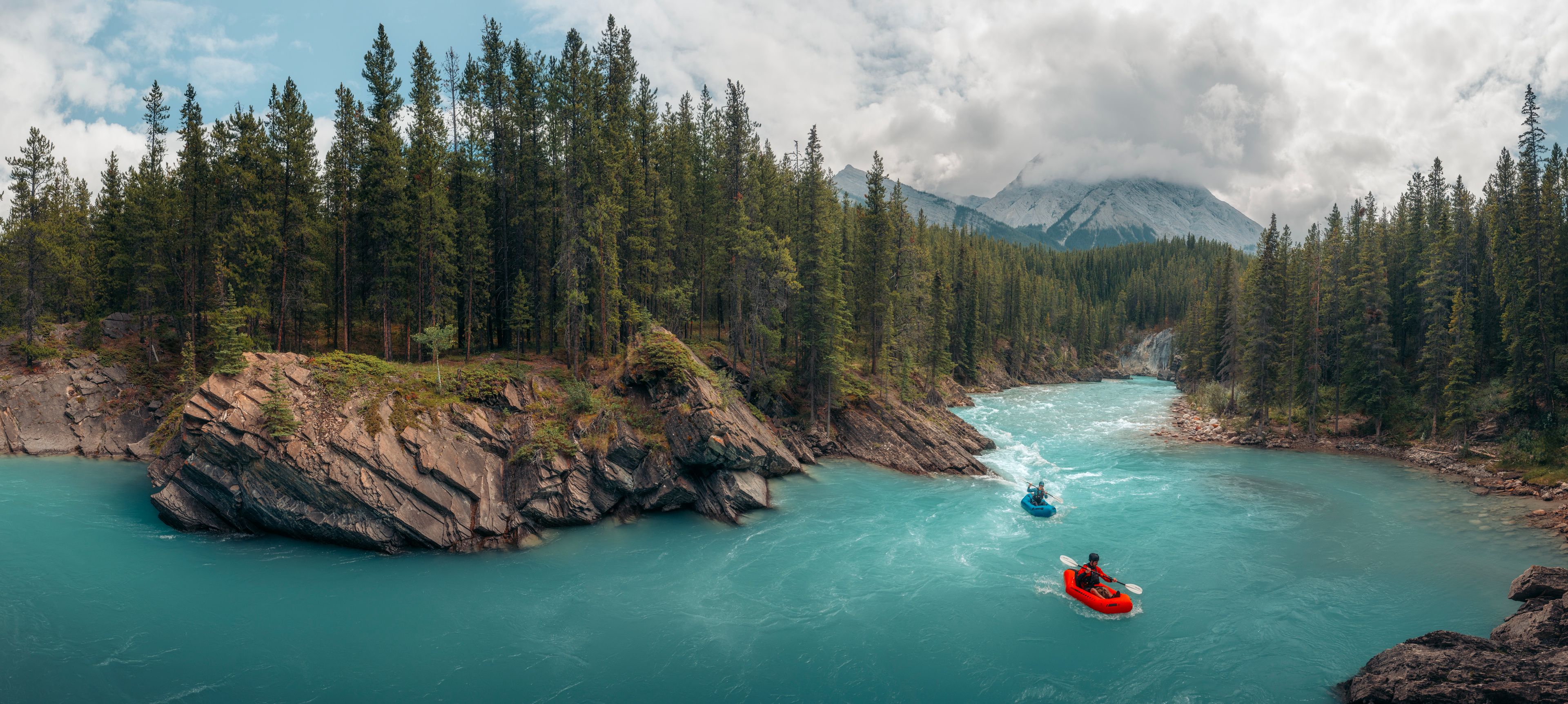 Two rafters float on the turquoise water of the Cline River with forests and mountains surrounding.