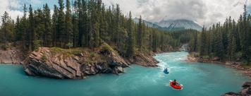 Two rafters float on the turquoise water of the Cline River with forests and mountains surrounding.