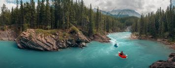 Two rafters float on the turquoise water of the Cline River with forests and mountains surrounding.