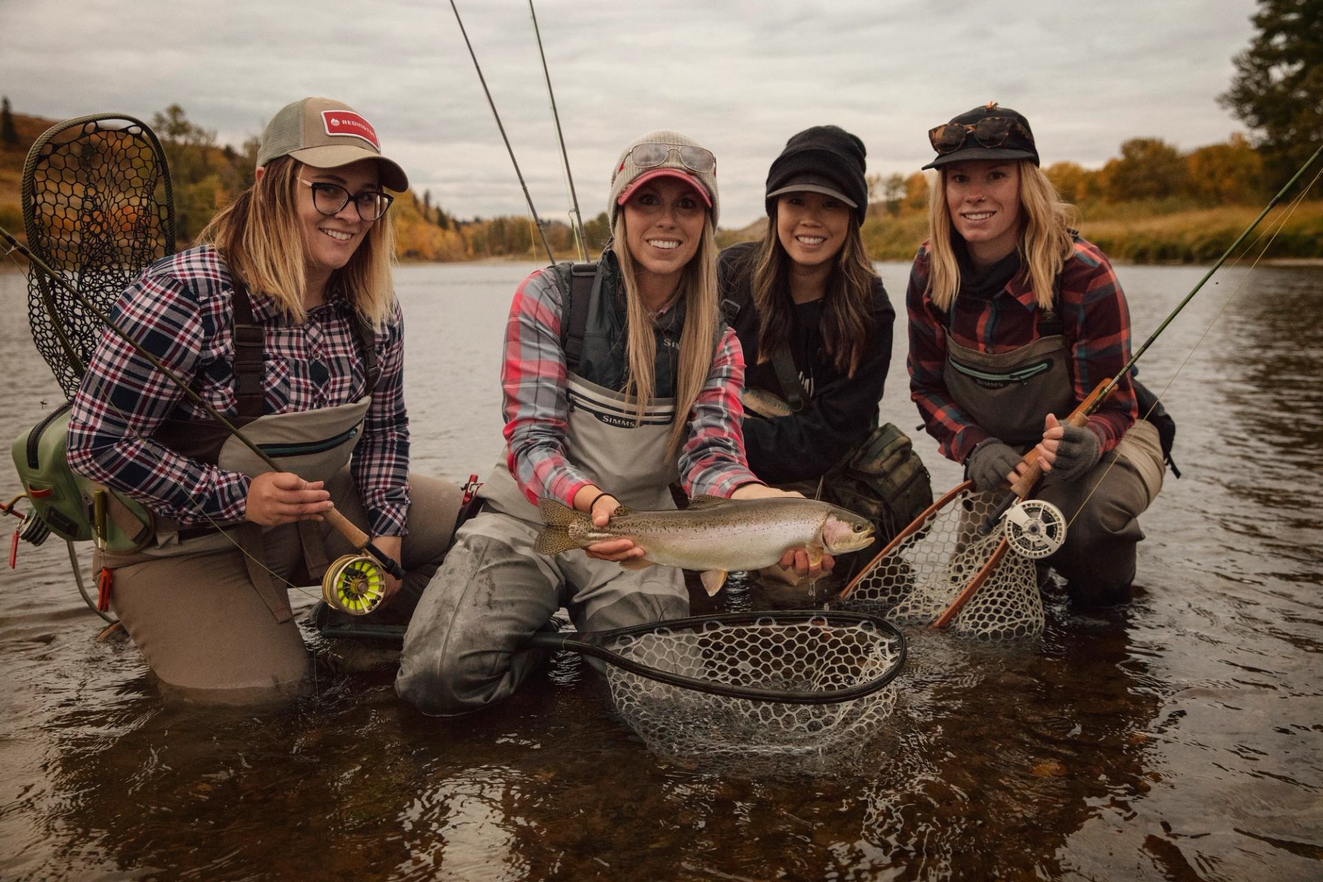 A group of women gather around a fish caught while fly fishing.