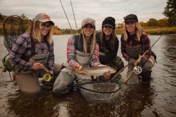 A group of women gather around a fish caught while fly fishing.