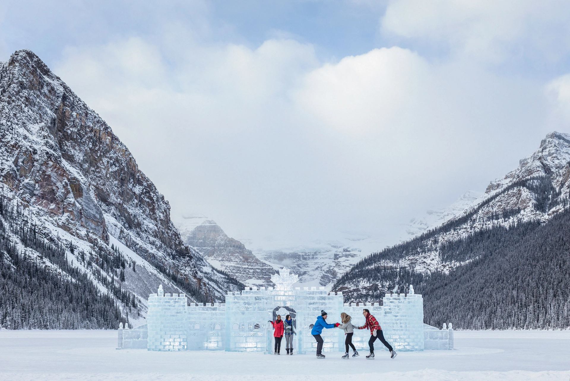 A group of people skating around the ice castle on Lake Louise with the Victoria Glacier and the Canadian Rockies in the background.