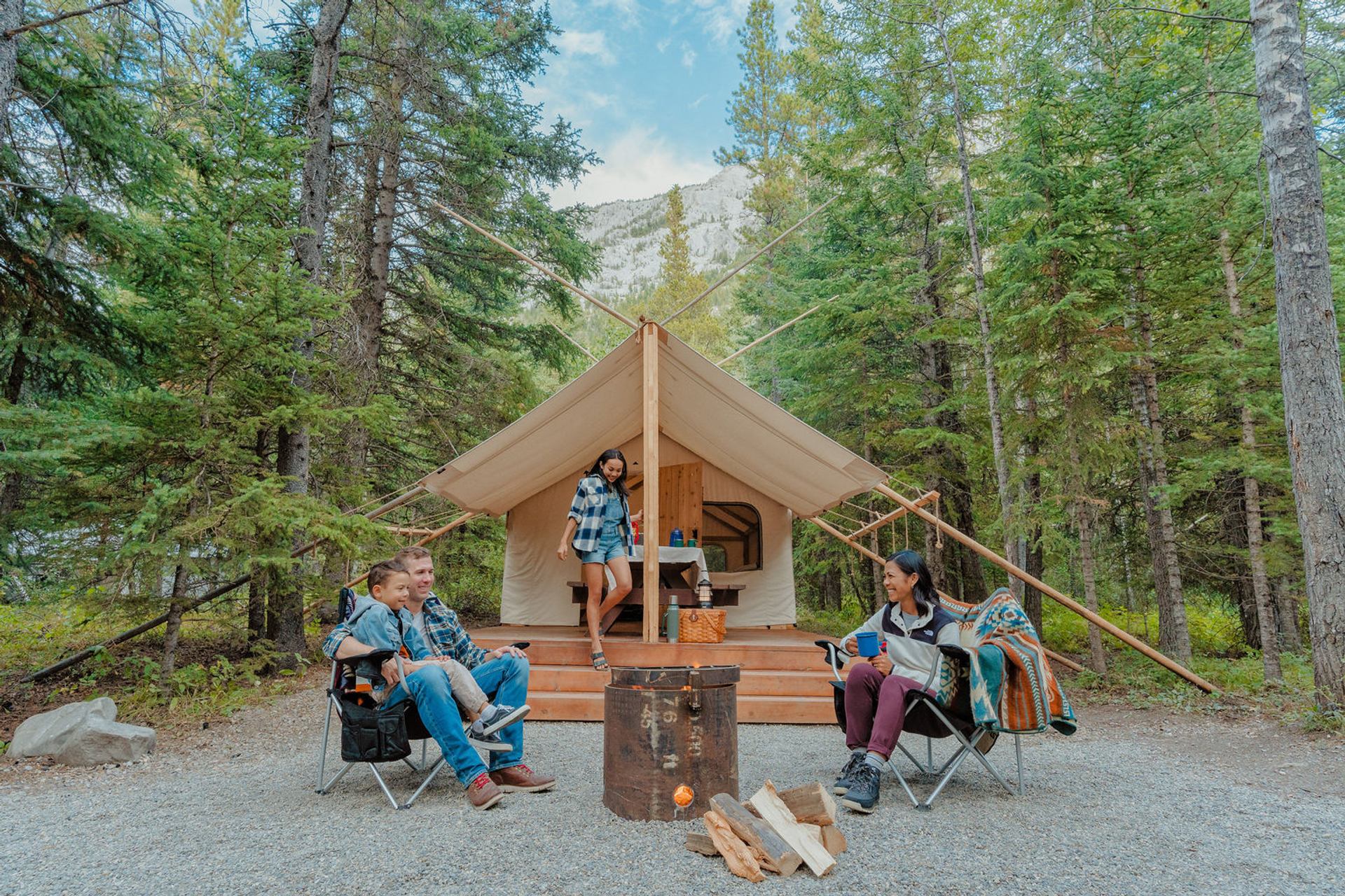 A family sits around a fire in front of trapper's tent in the forest