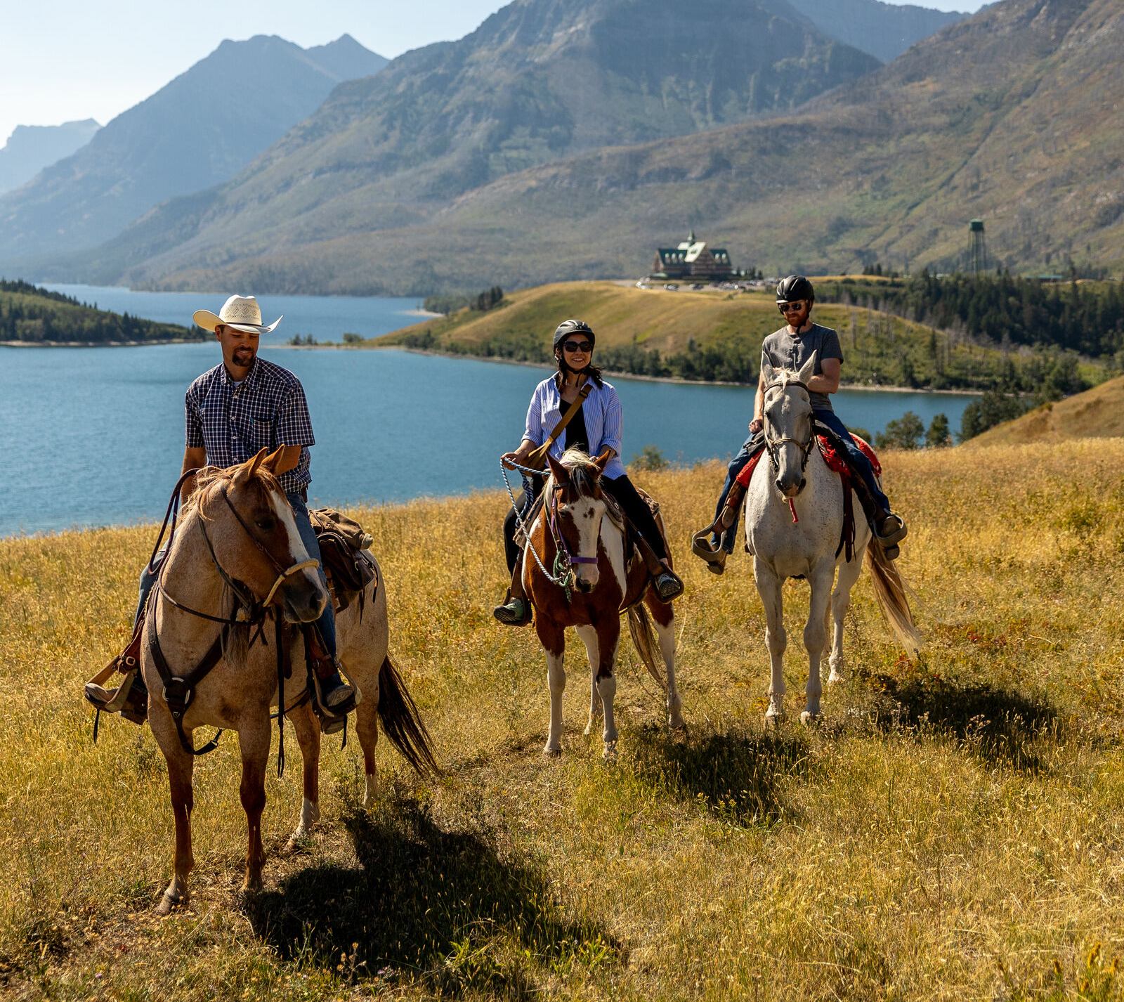 Trailriders stop with their horses in Waterton Lakes National Park with mountains surrounding them.