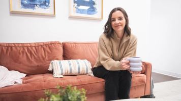 Women sits on a couch with a coffee mug in her hand.