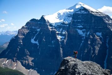 View of a climber far away reaching a summit with a larger mountain peak in the background.