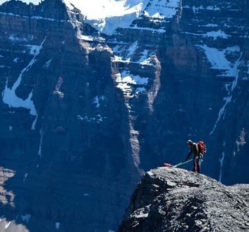 View of a climber far away reaching a summit with a larger mountain peak in the background.
