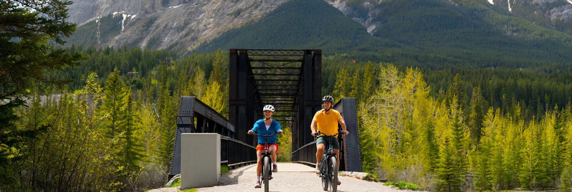 A couple riding their bikes across the Canmore Engine Bridge.