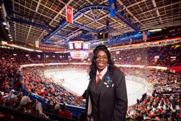 Arena employee smiling at a hockey game with the stands filled with spectators.