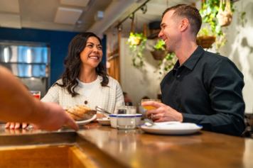 Man and woman share drinks at the bar while being served food from over the bar.