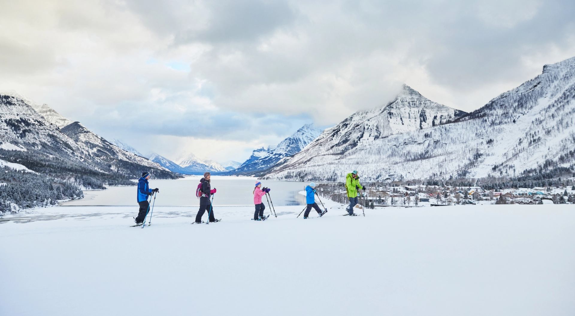 A family of two parents and two children following a guide on a snowshoe tour across a snow covered valley in the mountains.