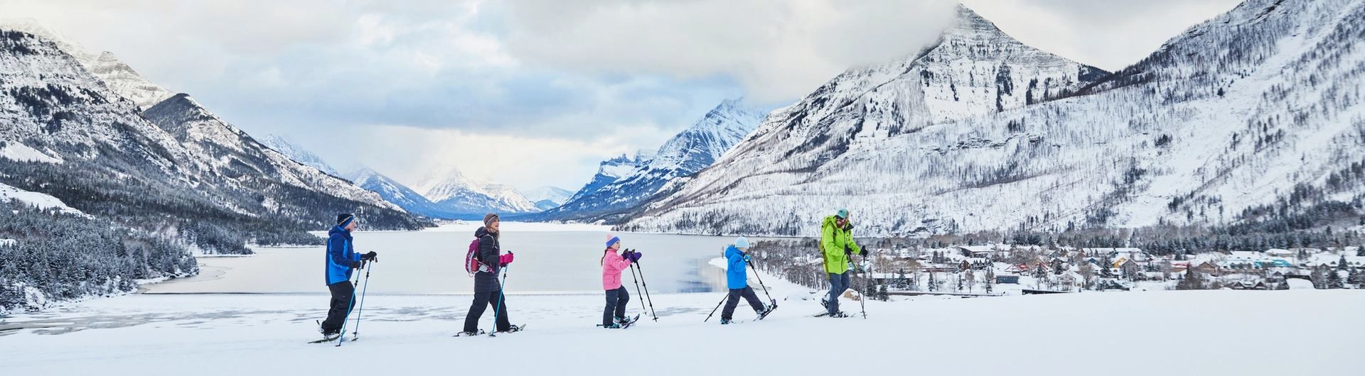 A family of two parents and two children following a guide on a snowshoe tour across a snow covered valley in the mountains.