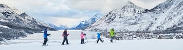 A family of two parents and two children following a guide on a snowshoe tour across a snow covered valley in the mountains.