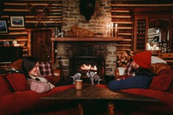 A couple sits in front of a stone fireplace in the log cabin lodge at Storm Mountain Lodge