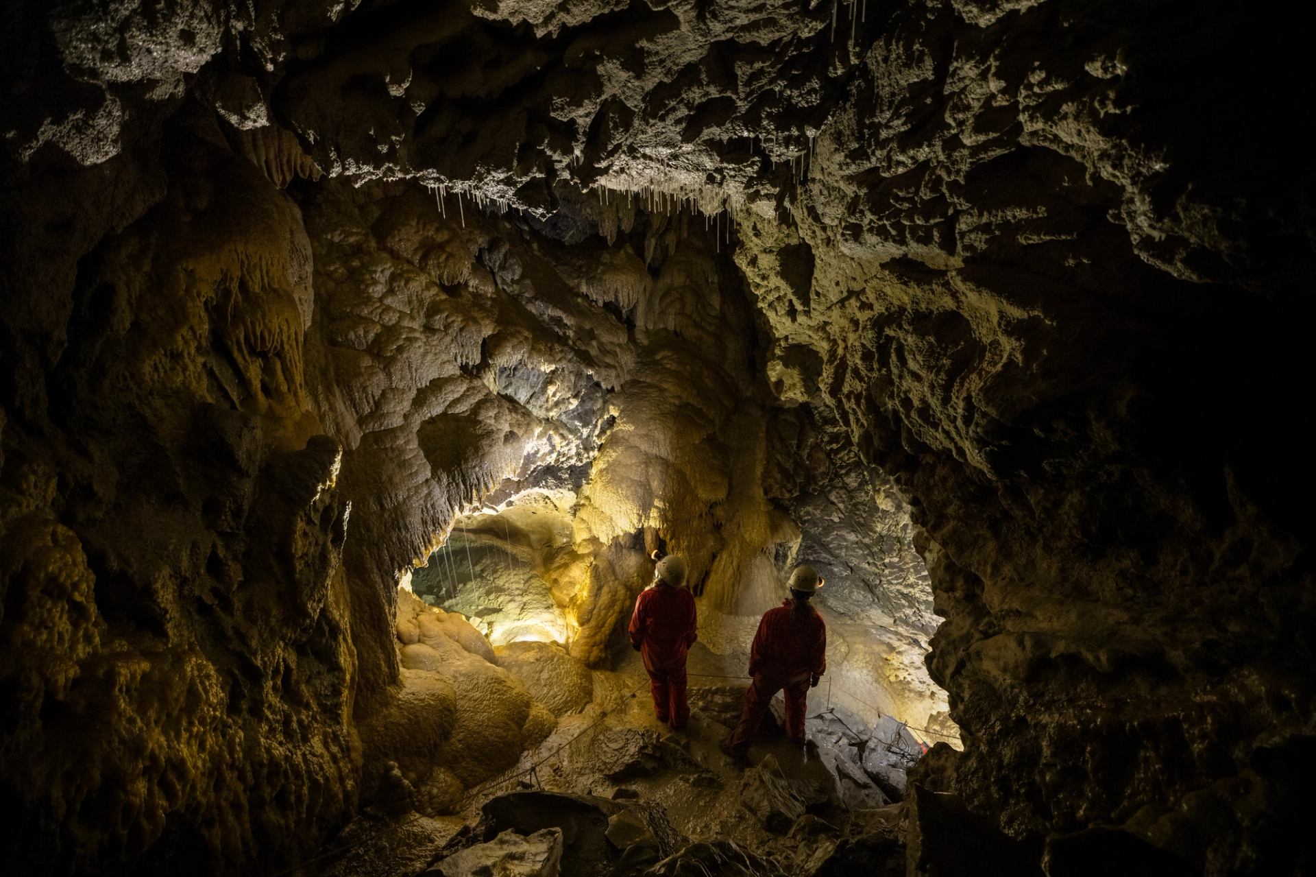 Two people shining their headlamps on the walls of a dark cave during a tour.