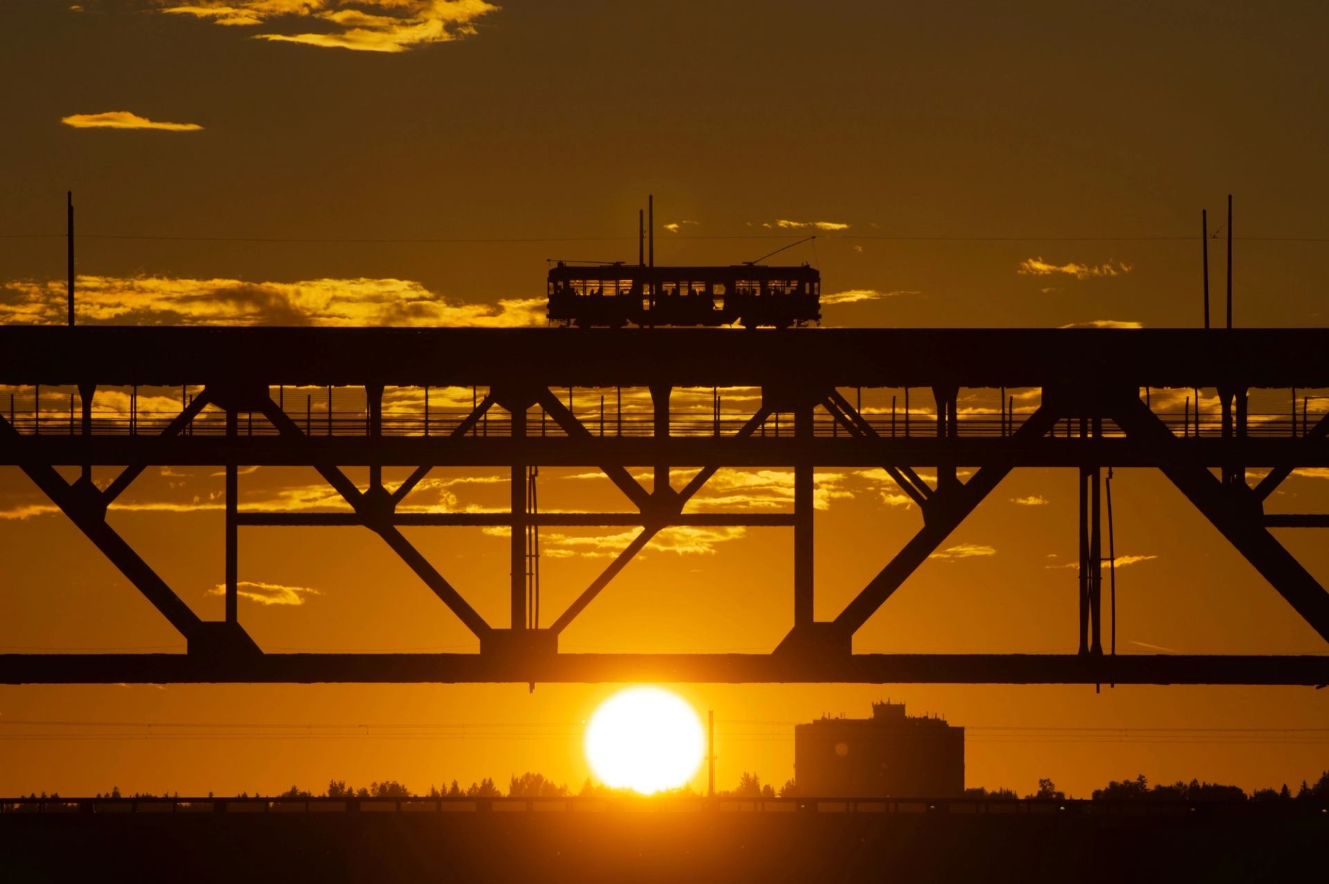 Edmonton's High Level Bridge Streetcar passes along a bridge as the orange sun glows in the background.
