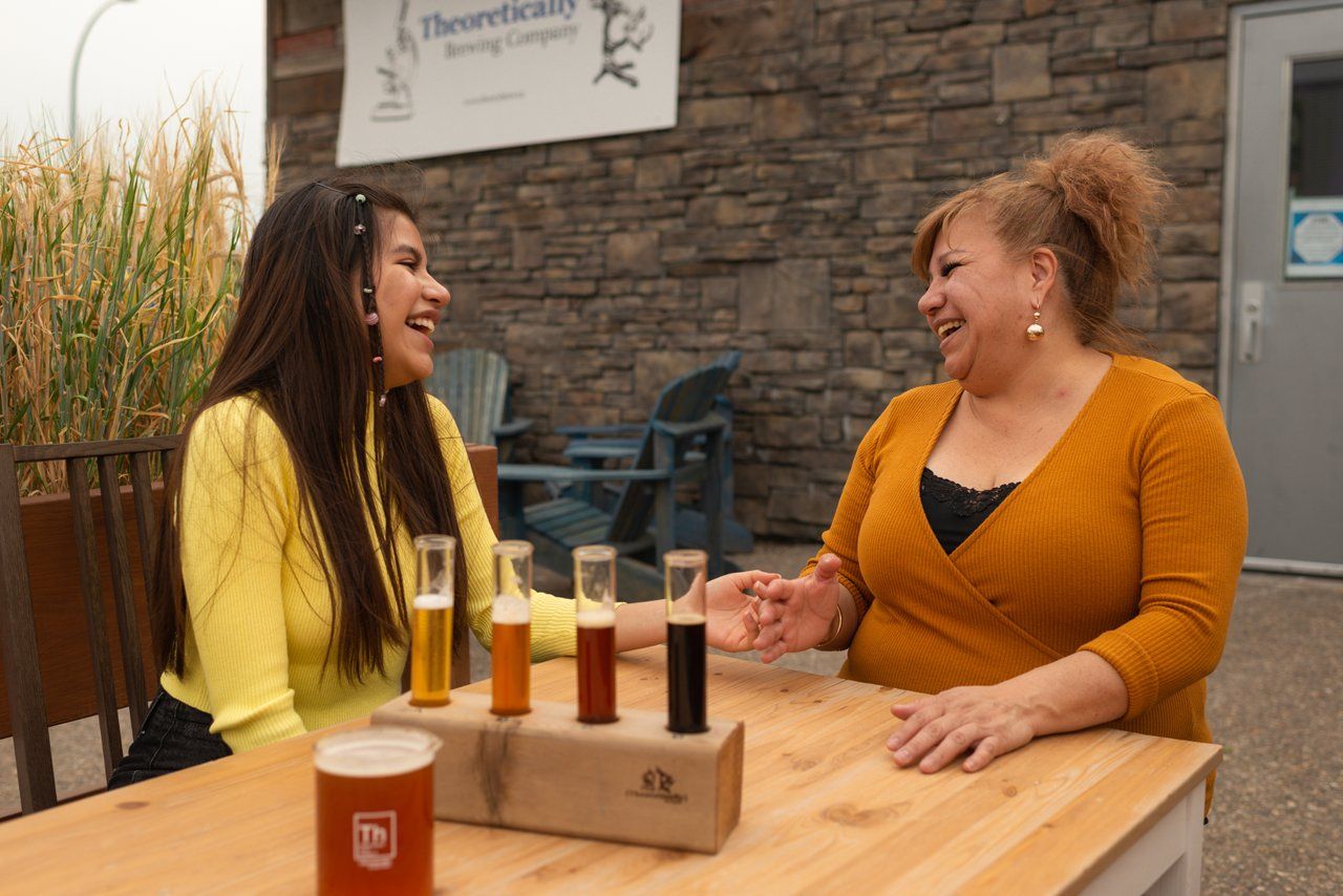 Two women laugh while enjoying a flight of beers on Theoretically Brewing Co.'s patio in Lethbridge.