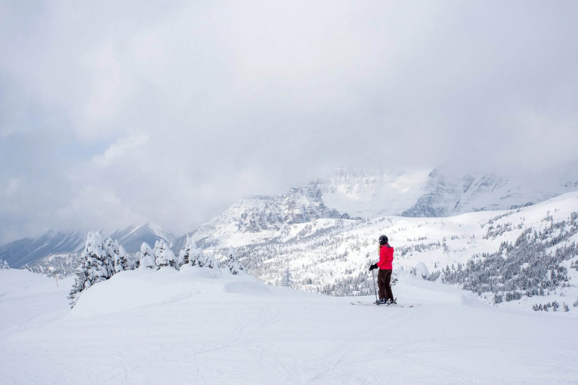 A solo skier stands at the top of Standish Chair, taking in loads of powder and mountains in the distance at Sunshine Village in Banff.