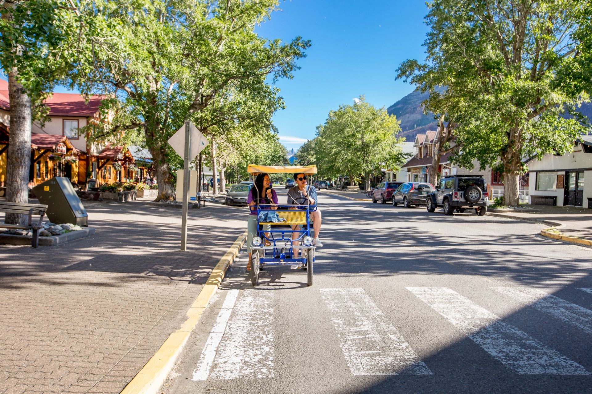 Couple on a two-seater tandem peddle bike driving down street in Waterton Lakes National Park.