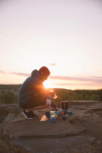 Man crouching beside hiking gear with sunrise in the background