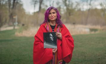 Indigenous women looking at camera while holding a black and white photo.
