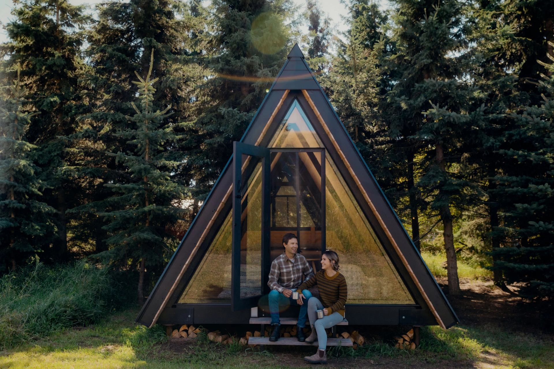 A couple sits outside their A-frame cabin at Pine Creek Resort in the boreal forest.
