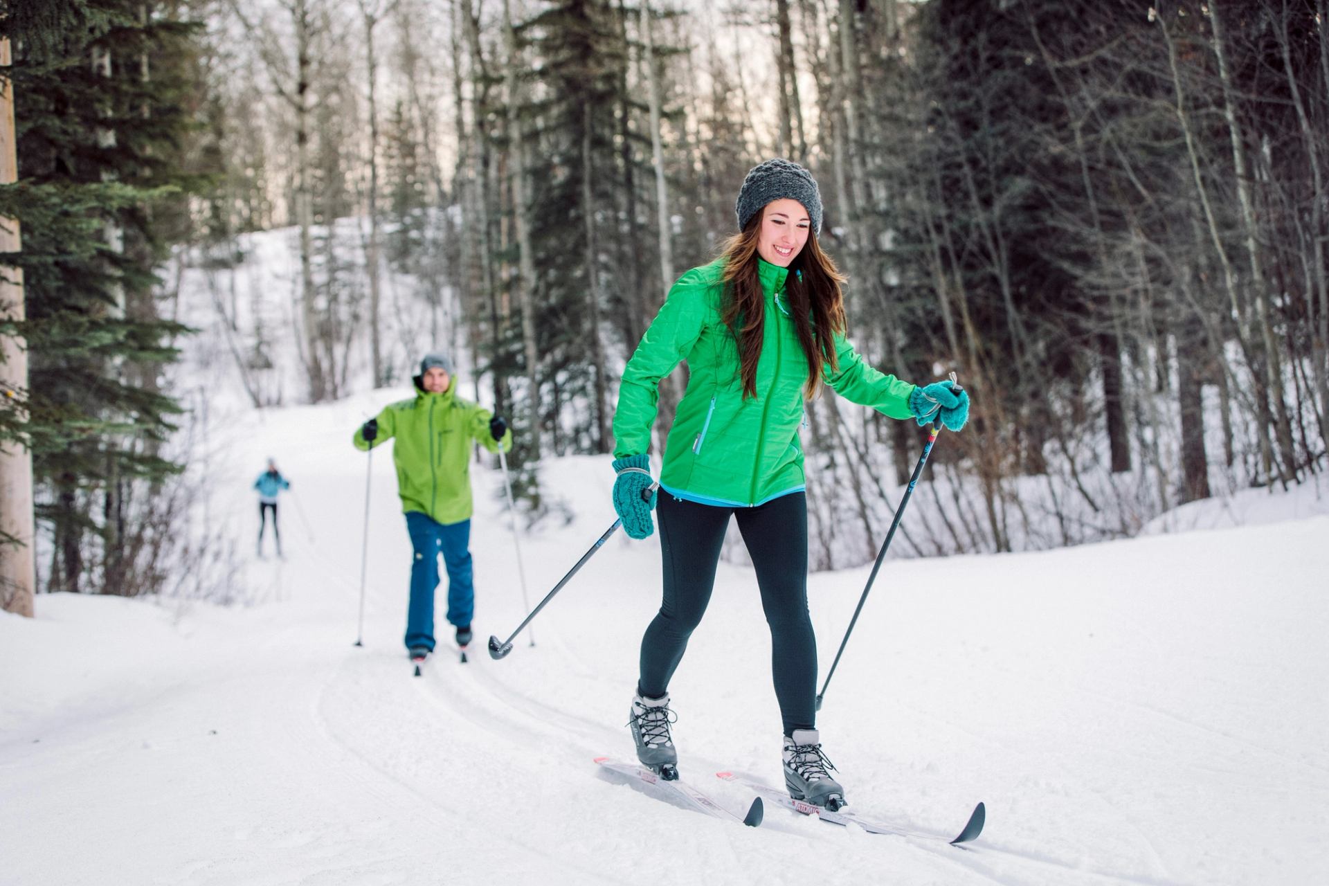 People cross country skiing on a snowy trail through the trees.