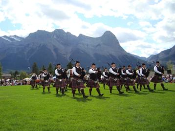 Bagpipers in a formation during an outdoor performance with mountains in the background.