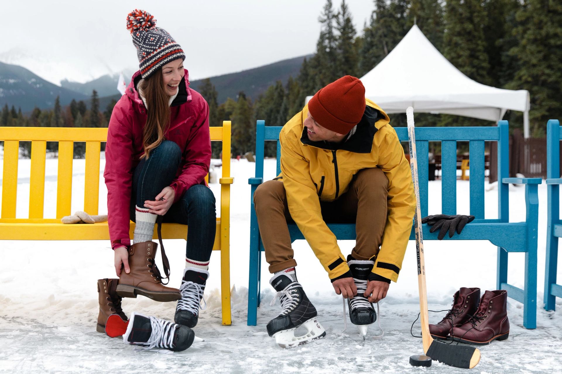 Two people sitting on a bench and putting on their ice skates at the Fairmont Jasper Park Lodge's outdoor skating rink.