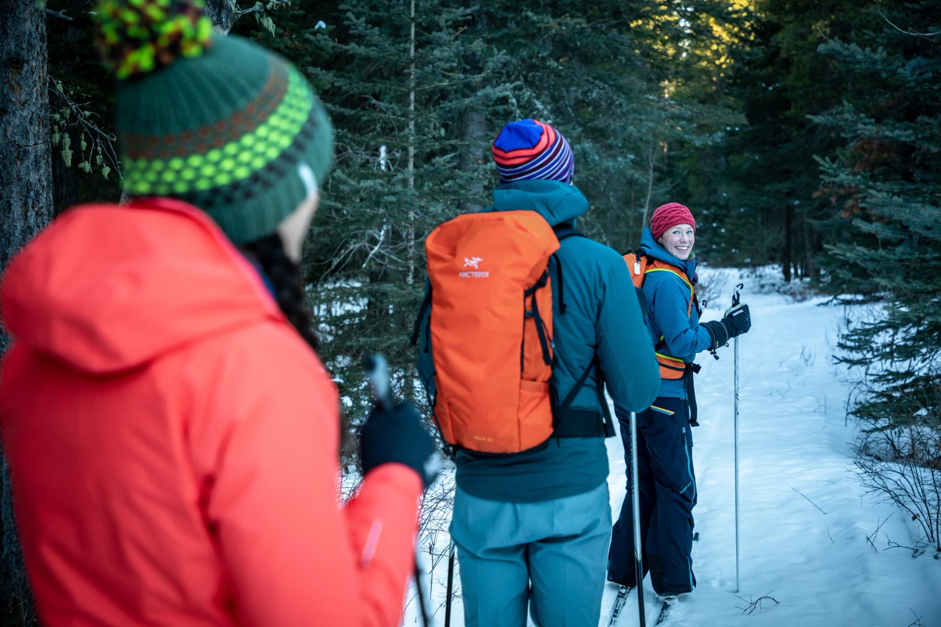 Three people cross country skiing on a trail with trees.