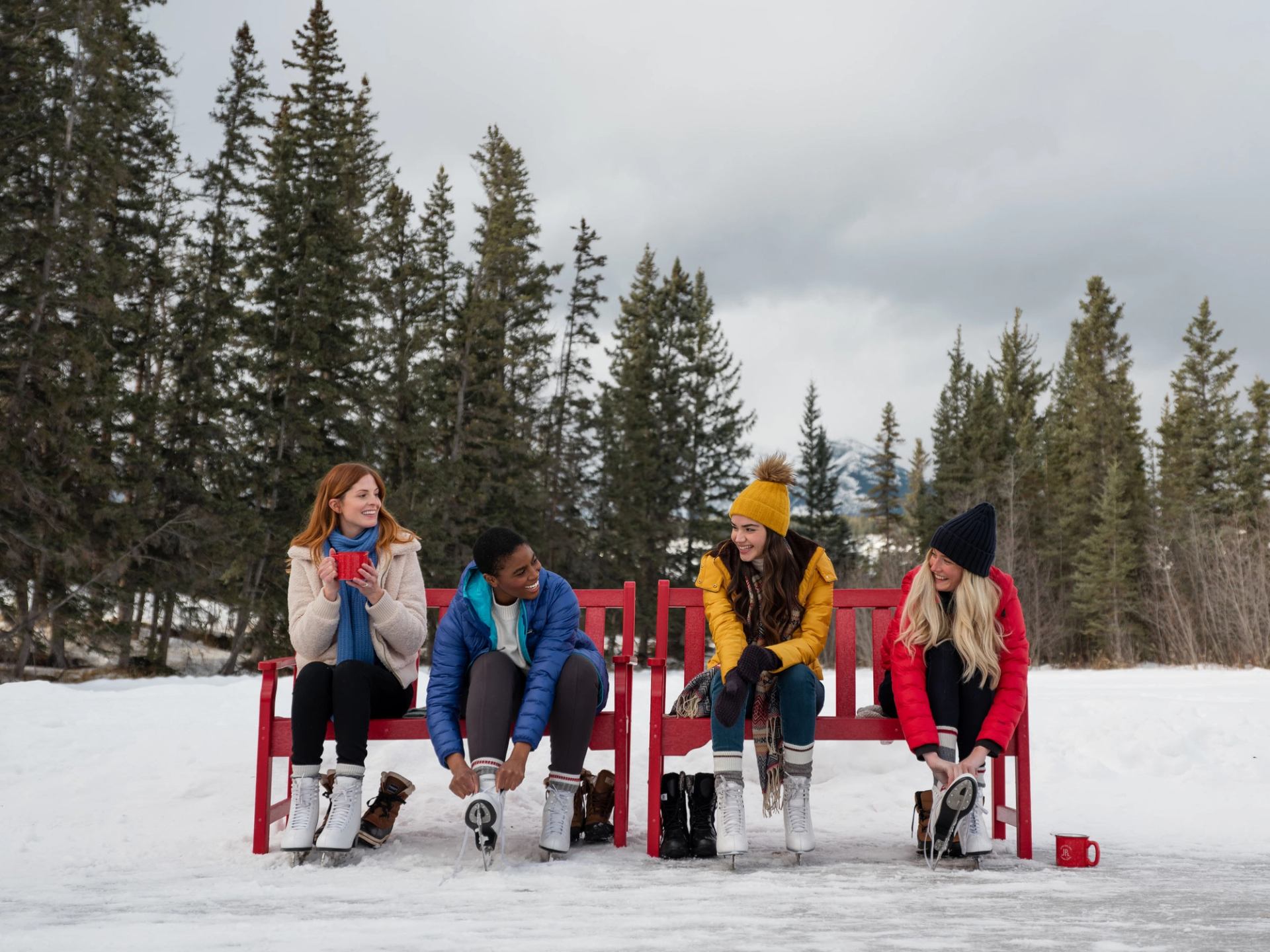 A group of four friends sit on a bench lacing up their ice skates at the Fairmont Jasper Park Lodge in Jasper National Park.