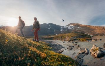 Two Heli Hikers beginning their hike with a helicopter taking off in background.