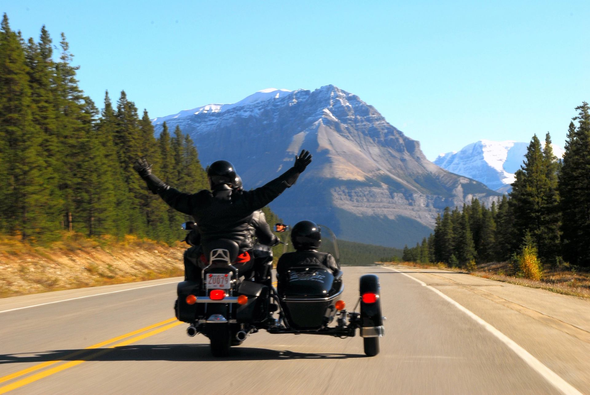 Three people on a motorcycle with sidecar driving through Jasper National Park on the Icefields Parkway.