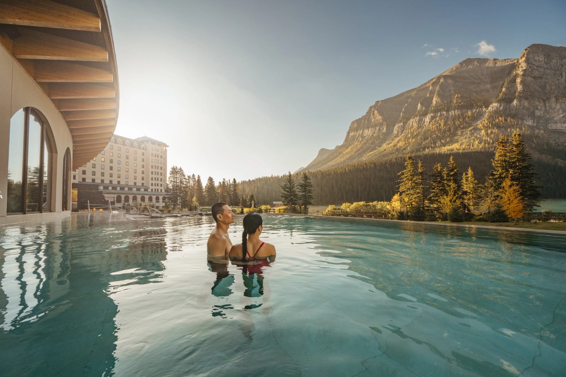 Bathers in the outdoor infinity pool at BASIN Glacial Waters are surrounded by mountains.