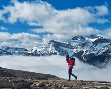 Woman hiking on a cliff with snow-capped mountain peaks in the background.