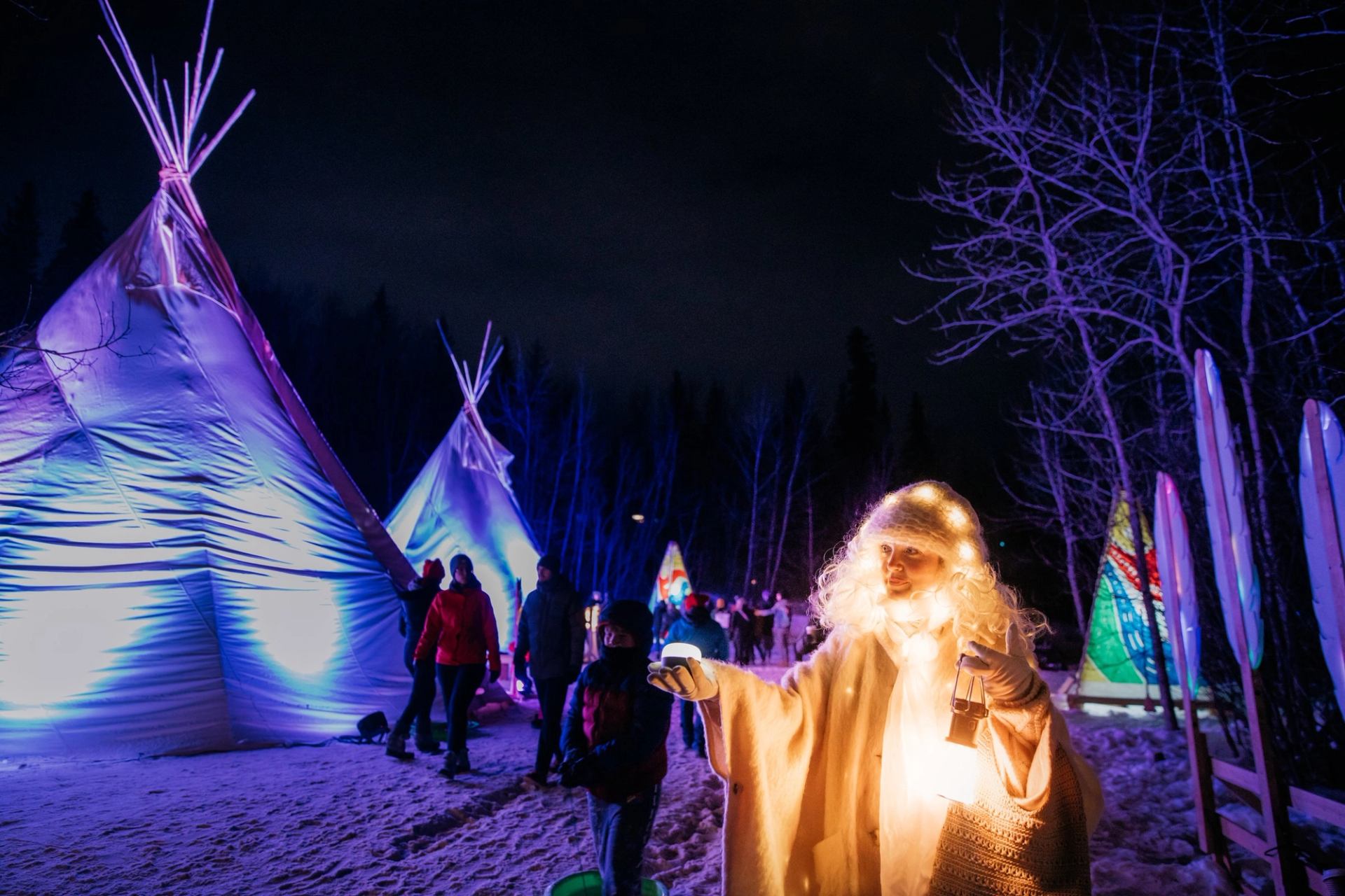 A glowing performer poses for a photo at night with colourful tipis in the background.