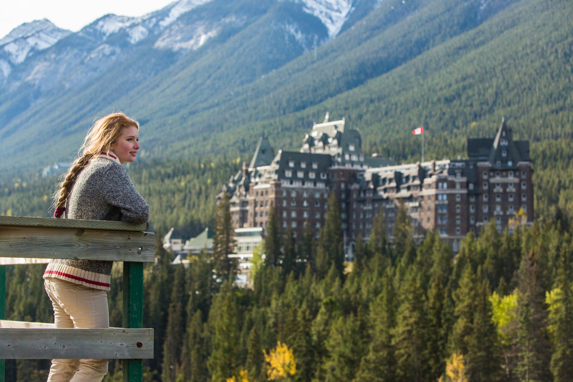 A woman looks out over a hotel and trees from a view platform.