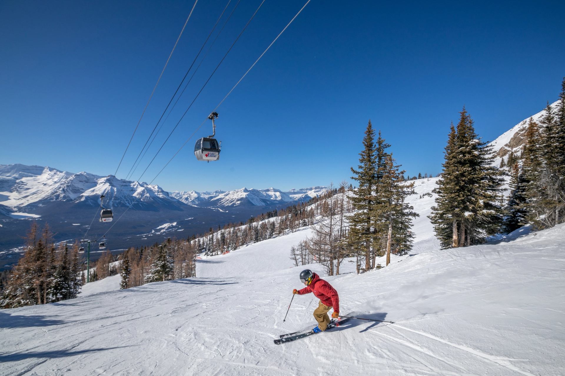 A skier skiing an intermediate groomed run directly under the chairlift, at Lake Louise Ski Resort in Banff National Park