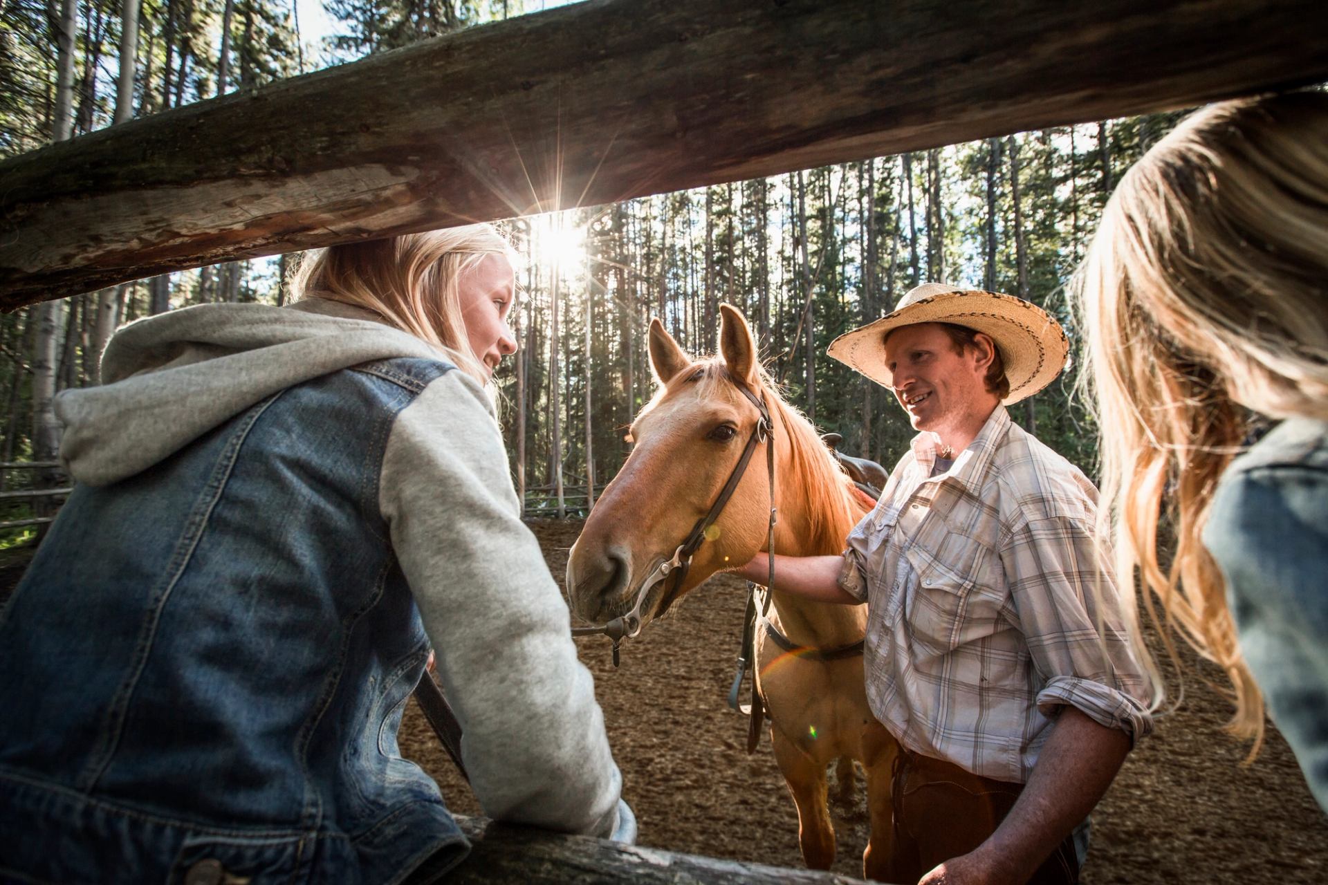 Two girls watching a cowboy holding a horse in a corral at Warner Stables in Banff National Park.