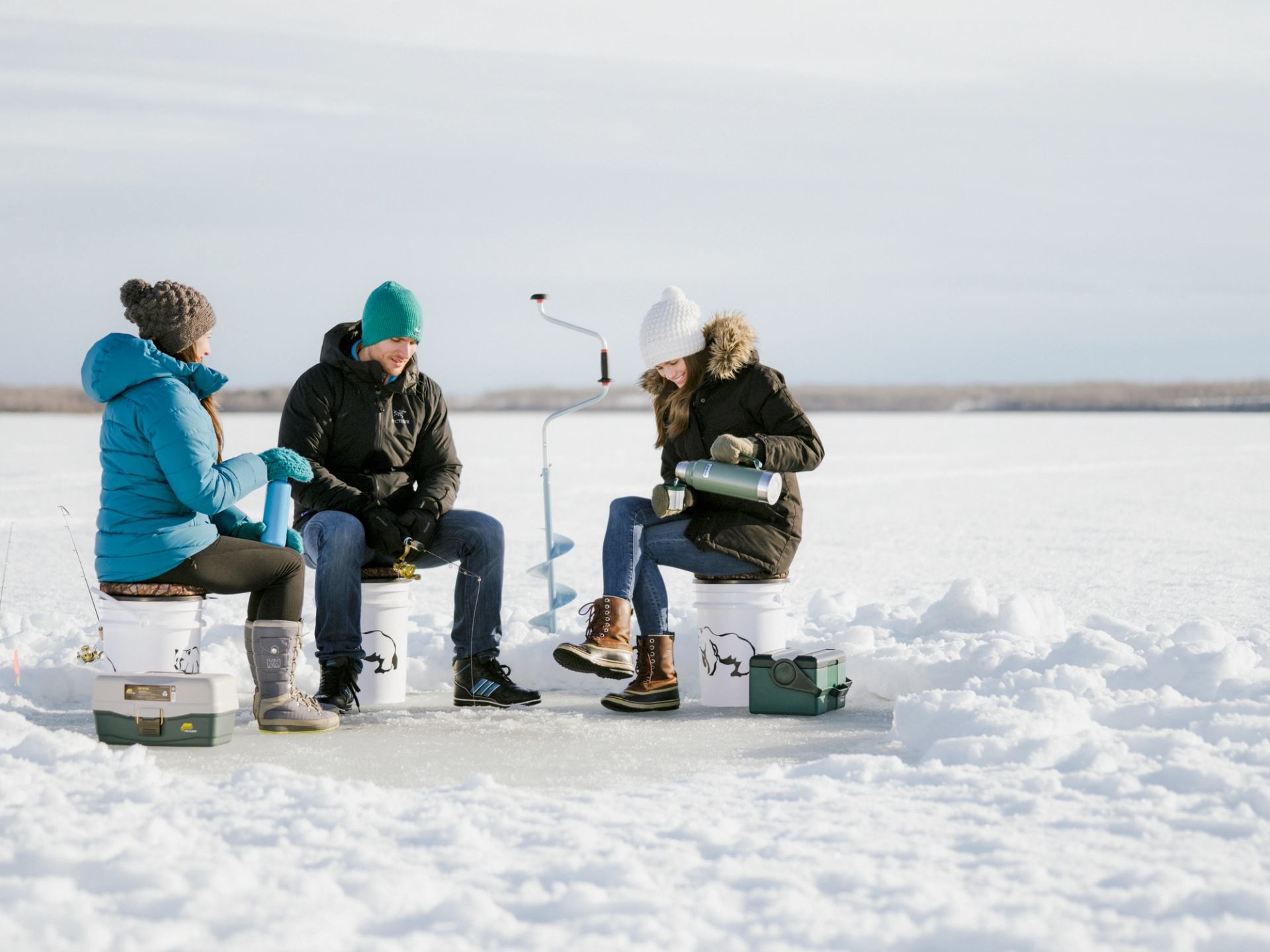 Friends enjoying a hot beverage while ice fishing on a frozen Bear Lake near Grande Prairie
