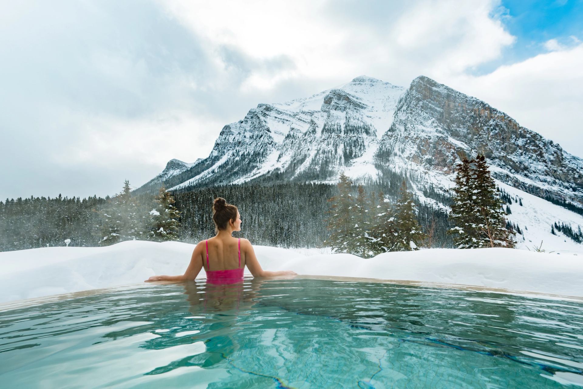 A woman enjoys the mountain view from an outdoor hot tub at BASIN Glacial Waters spa at Fairmont Chateau Lake Louise.