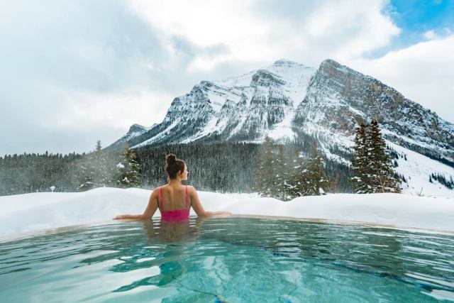 A woman enjoys the mountain view from an outdoor hot tub at BASIN Glacial Waters spa at Fairmont Chateau Lake Louise.