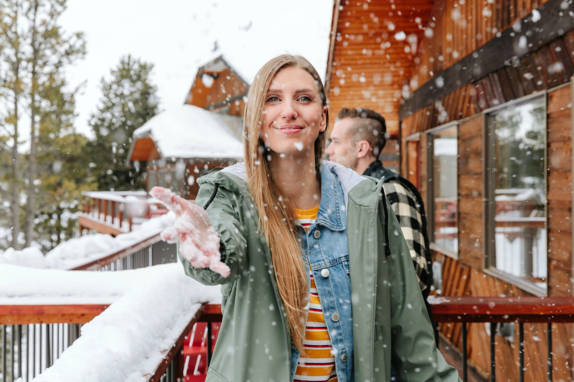 A woman standing on the deck of a log cabin catching snowflakes.