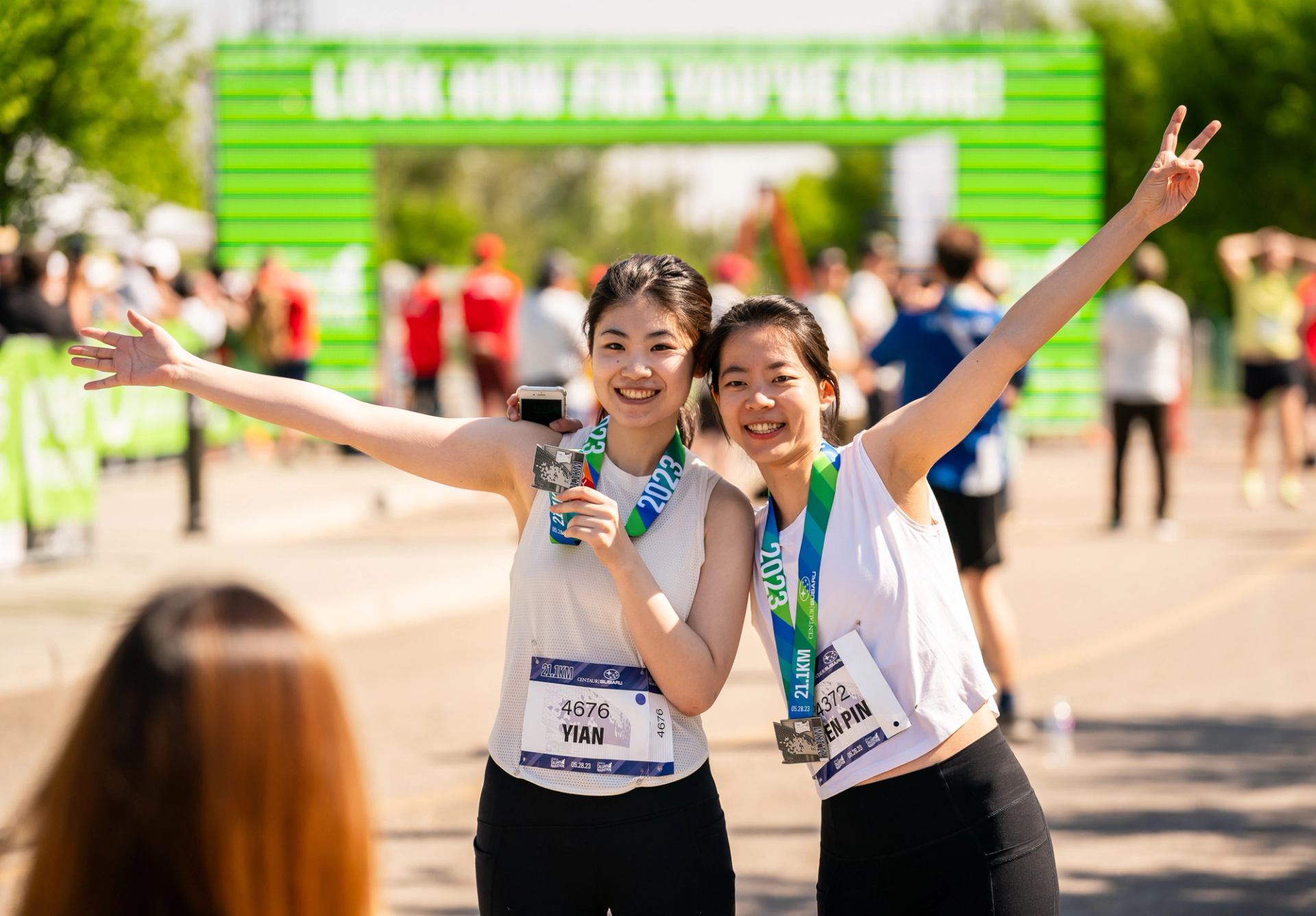 Two smiling runners show off their medals after running a half marathon at the Calgary Marathon.