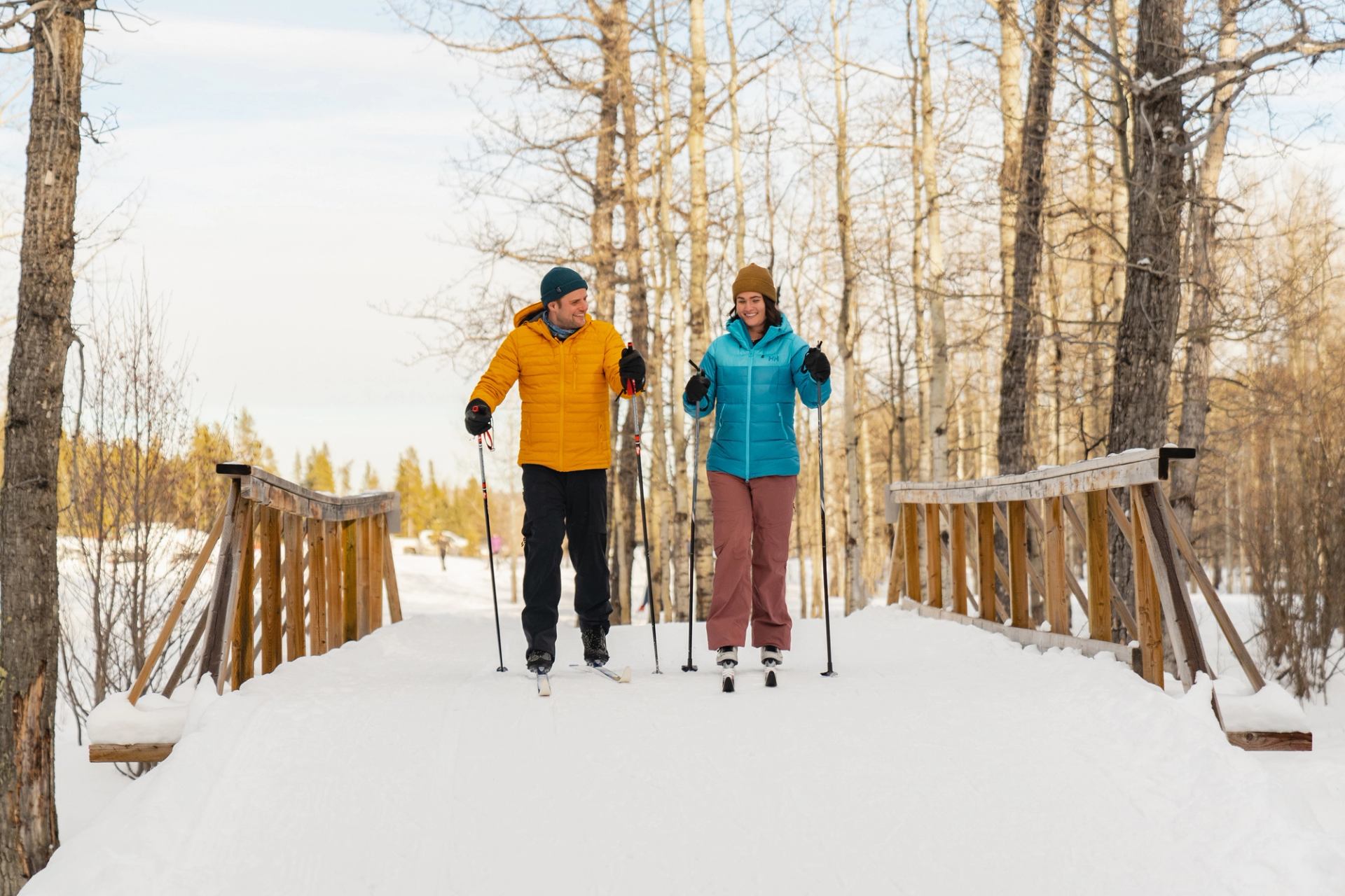 Two skiers crossing a bridge, enjoying the cross country ski trails while skiing in West Bragg Creek