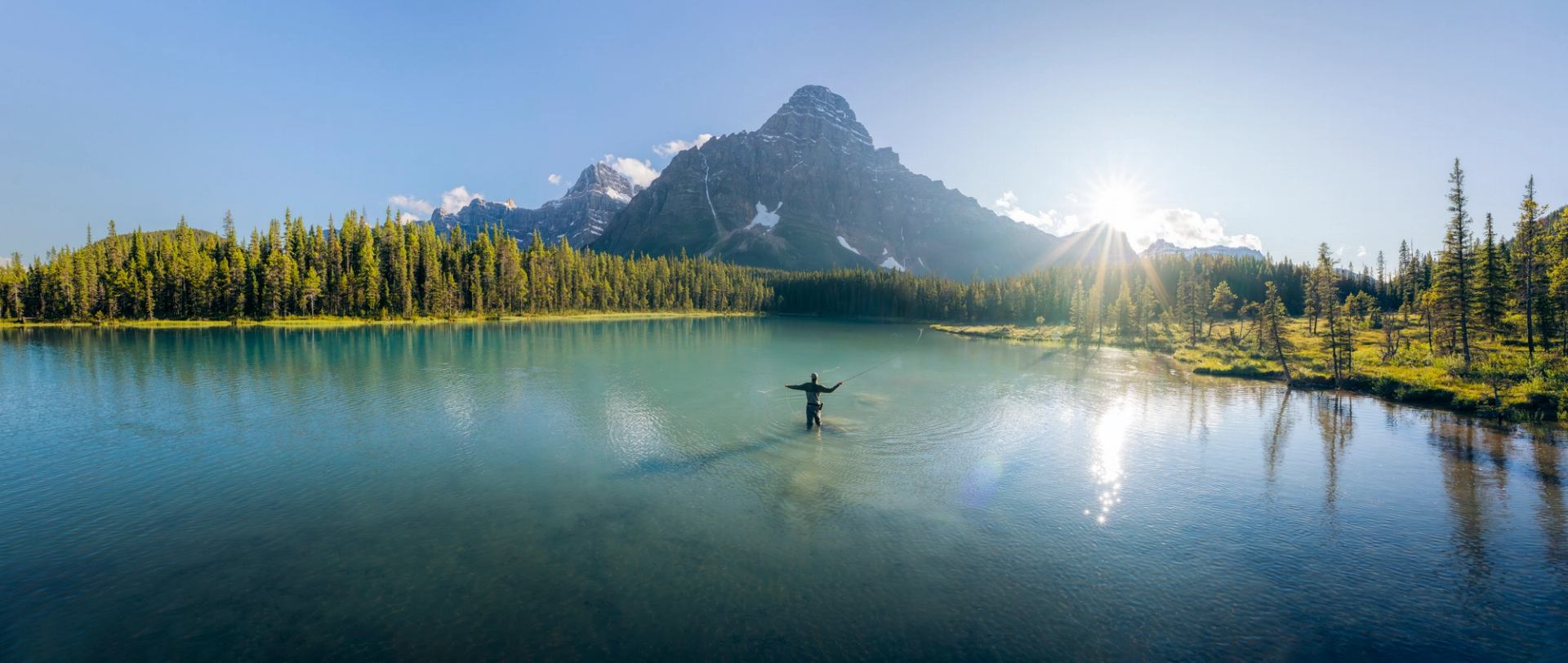 An angler casting his fishing rod into a still river.